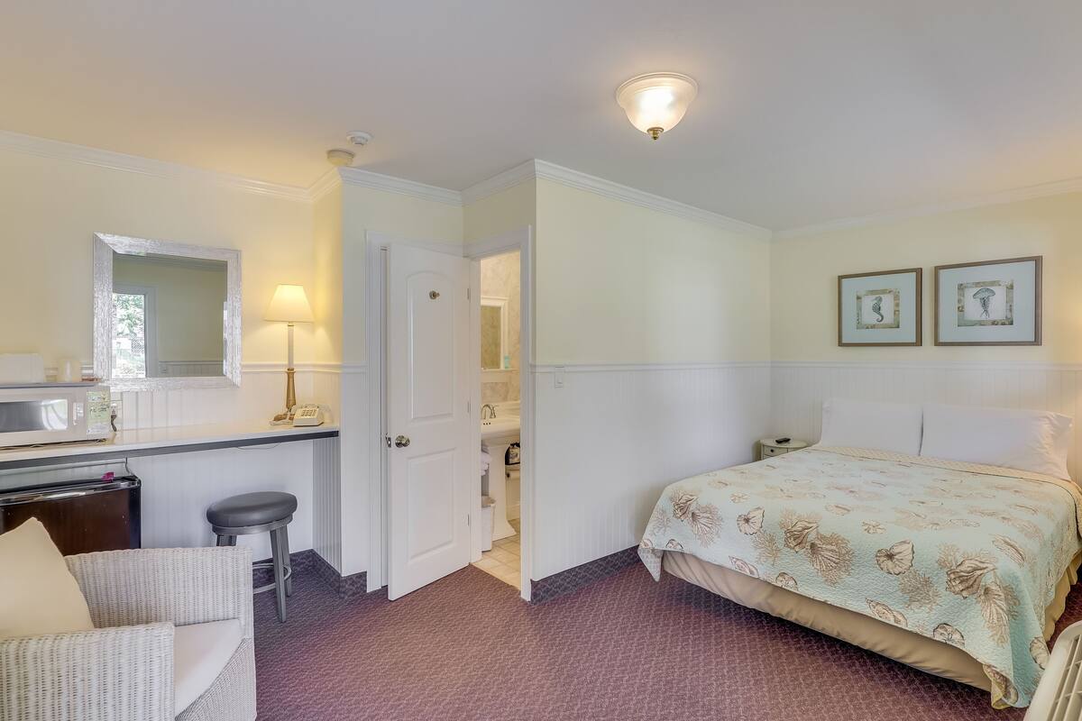 Une chambre à coucher comprenant un lit, un bureau, une chaise, un miroir et une porte donnant sur une salle de bain.