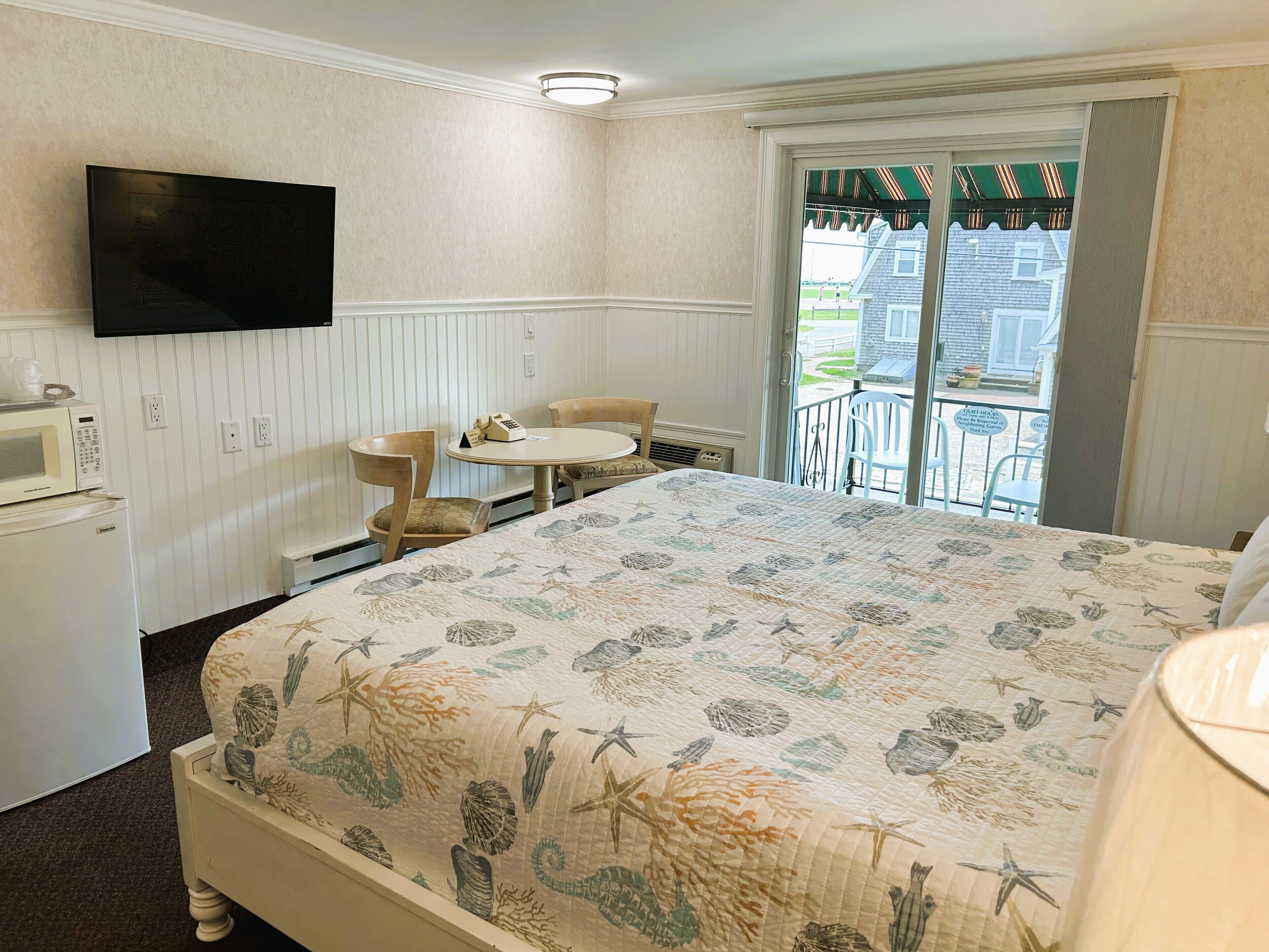 A hotel room with a bed, a desk, a chair, a microwave, and a television.