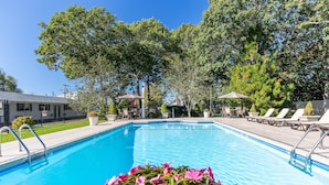 A swimming pool with lounge chairs and umbrellas, surrounded by trees and a building.