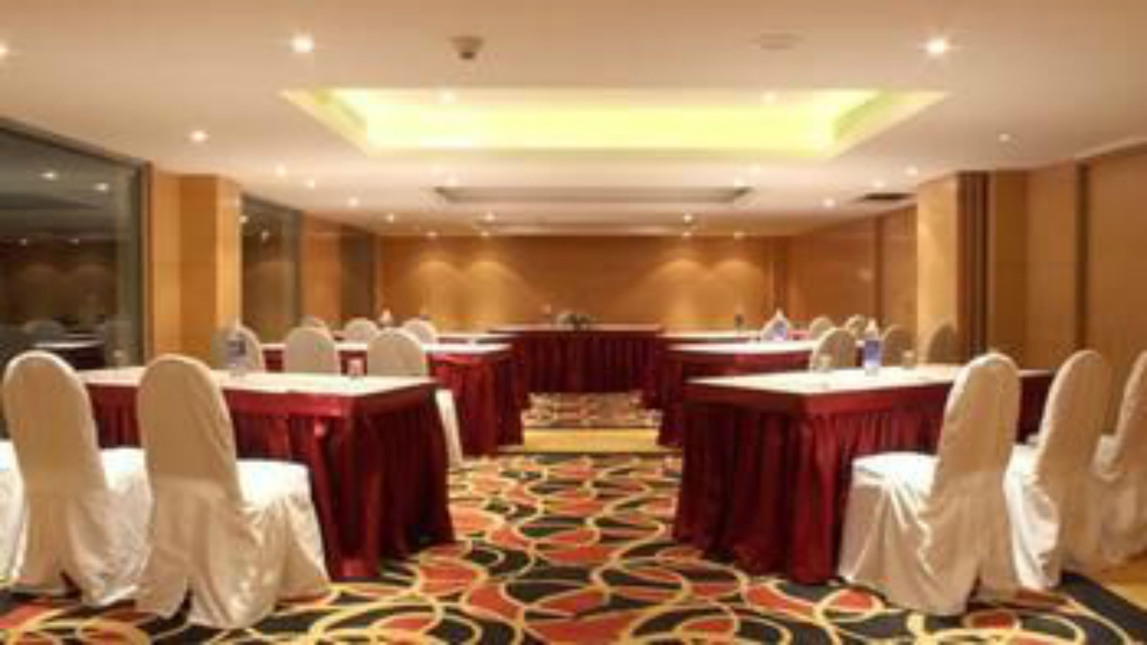 Un salón de conferencias con mesas y sillas, piso alfombrado e iluminación en el techo.