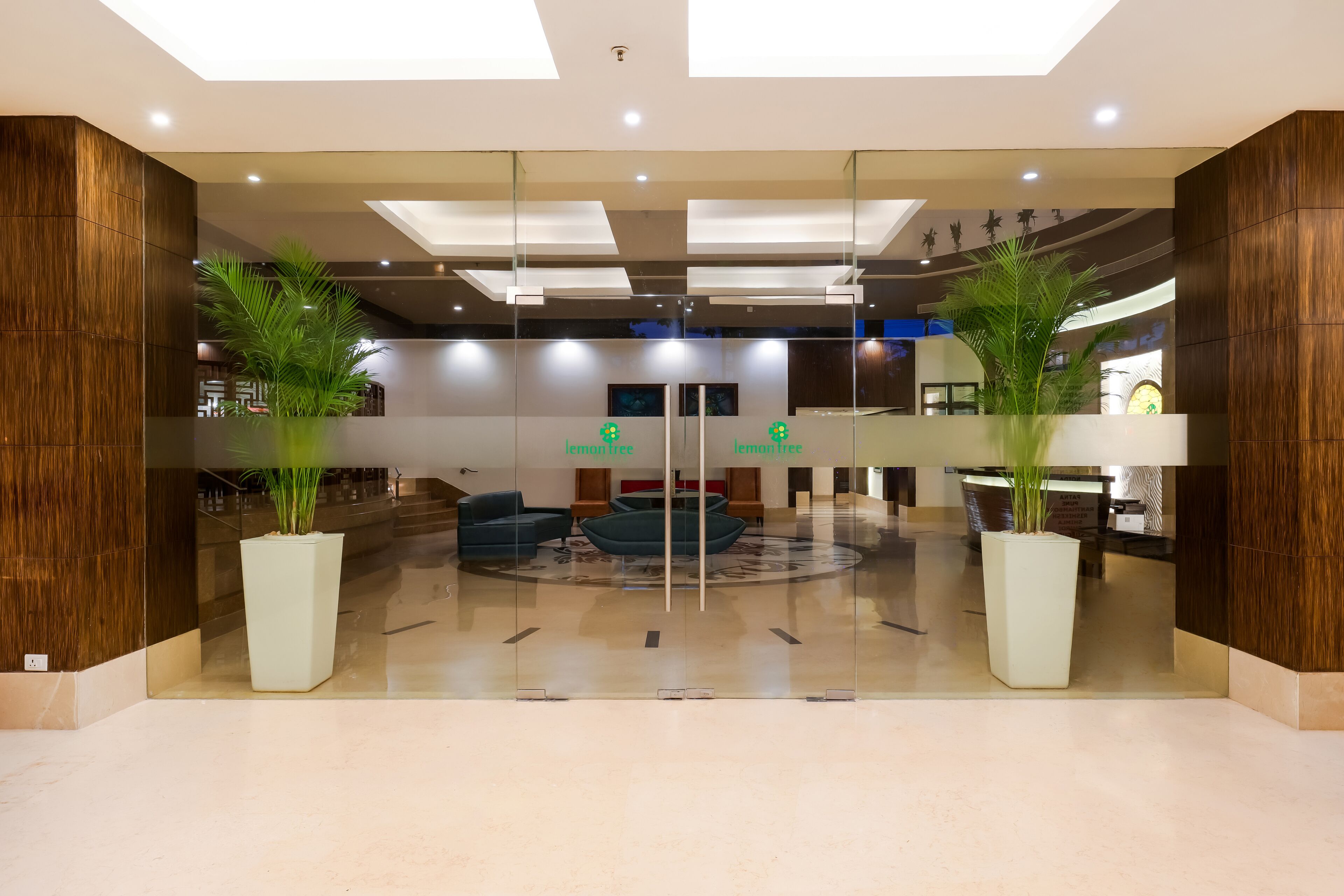 A modern lobby with glass walls, a central seating area, and large potted plants.