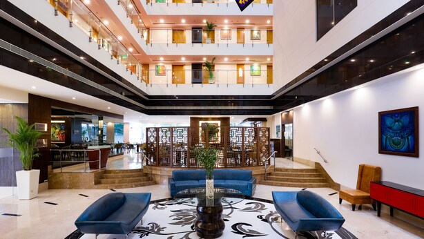 Vestíbulo de hotel de varios niveles con una zona de estar central, una escalera y un área de comedor al fondo.