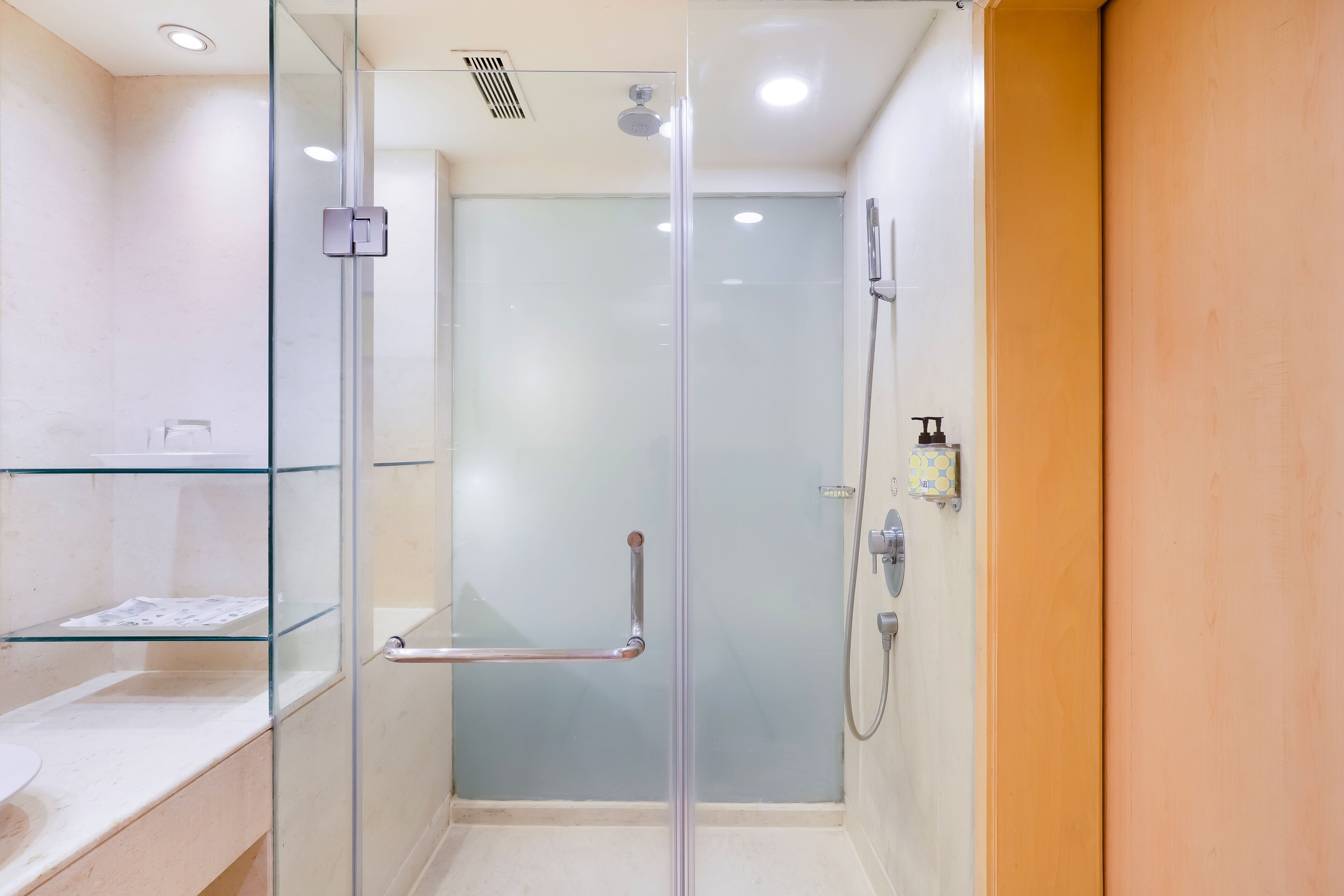 A modern bathroom with a glass-enclosed shower, a glass shelf, and a wooden door.