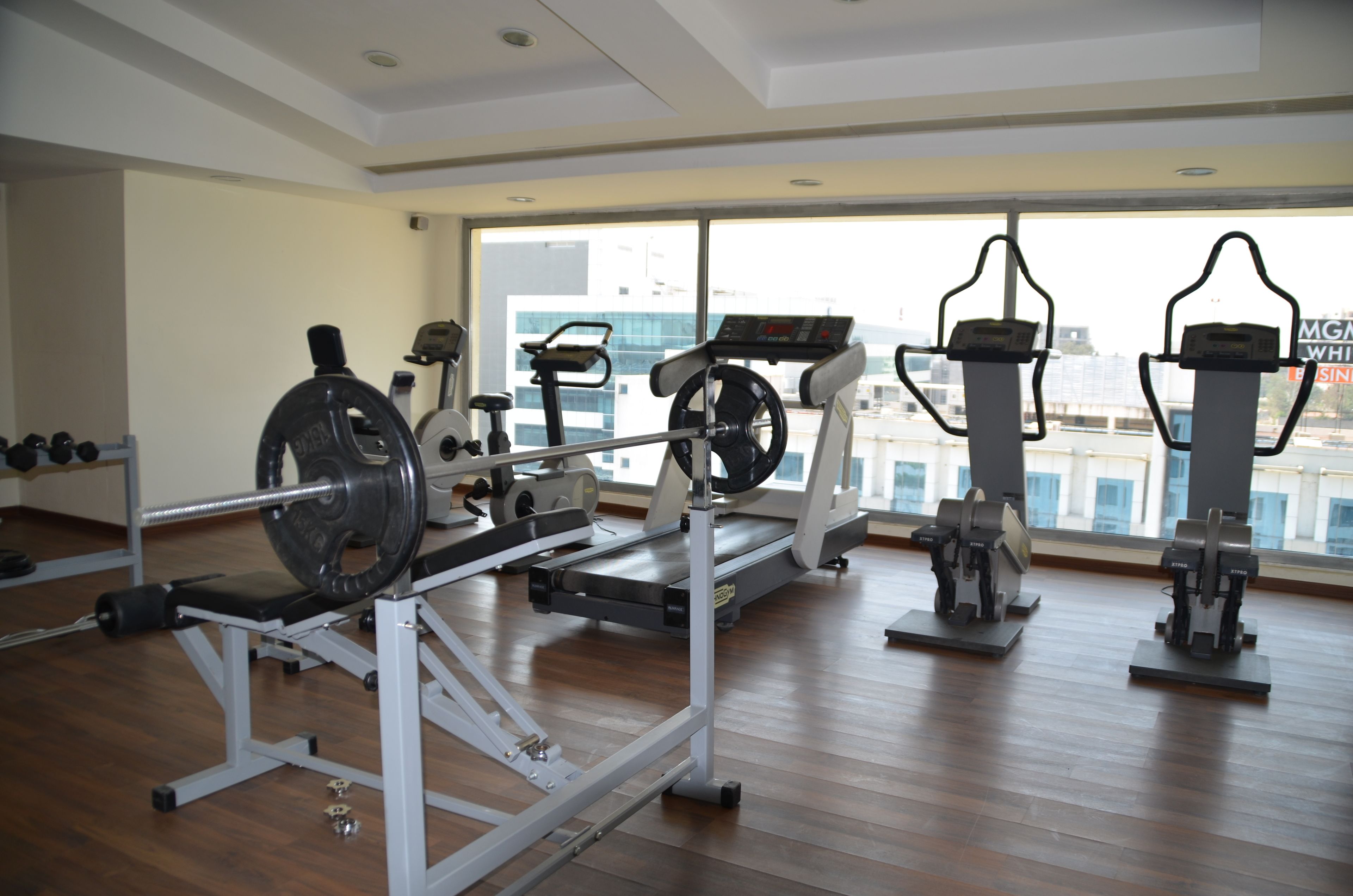 A gym with cardio machines, weightlifting equipment, and a large window with a city view.