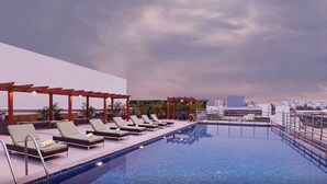Piscina en la azotea con sillones reclinables y una pérgola, con vistas a un paisaje urbano.