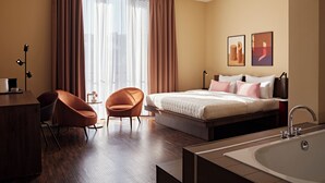 Une chambre d’hôtel moderne équipée d’un lit, d’un bureau, d’une chaise, d’une grande fenêtre avec des rideaux, d’un lavabo et de deux œuvres d’art accrochées au mur.