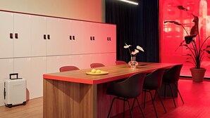 Une salle de conférence moderne, avec une table en bois, des chaises noires, une plante en pot et un mur d’accent rouge.