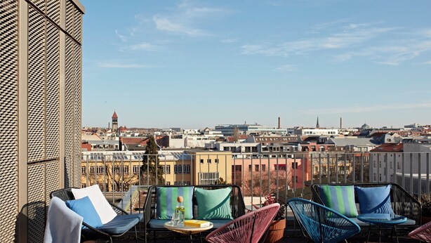 Une terrasse avec des sièges extérieurs, une vue sur le paysage urbain et un bâtiment à la façade ornée de motifs.