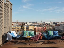 Eine Terrasse mit Außenbestuhlung, Blick auf eine Stadtlandschaft und ein Gebäude mit einem gemusterten Fassade.