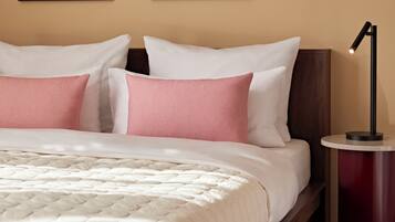 A neatly made bed with a white and pink color scheme, a bedside table with a lamp, and two abstract paintings on the wall.