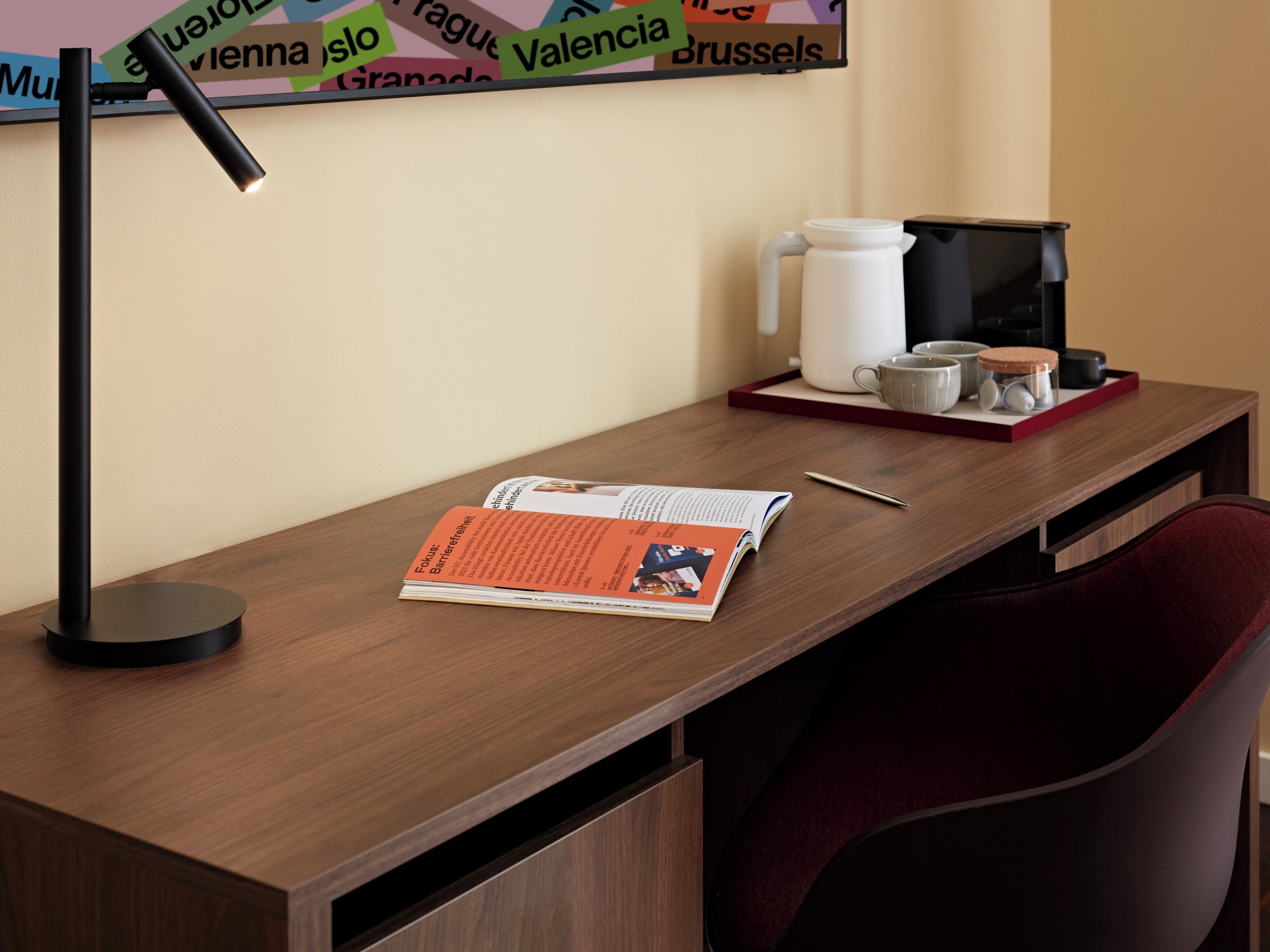 A wooden desk with a magazine, a pen, a coffee maker, and a cup.