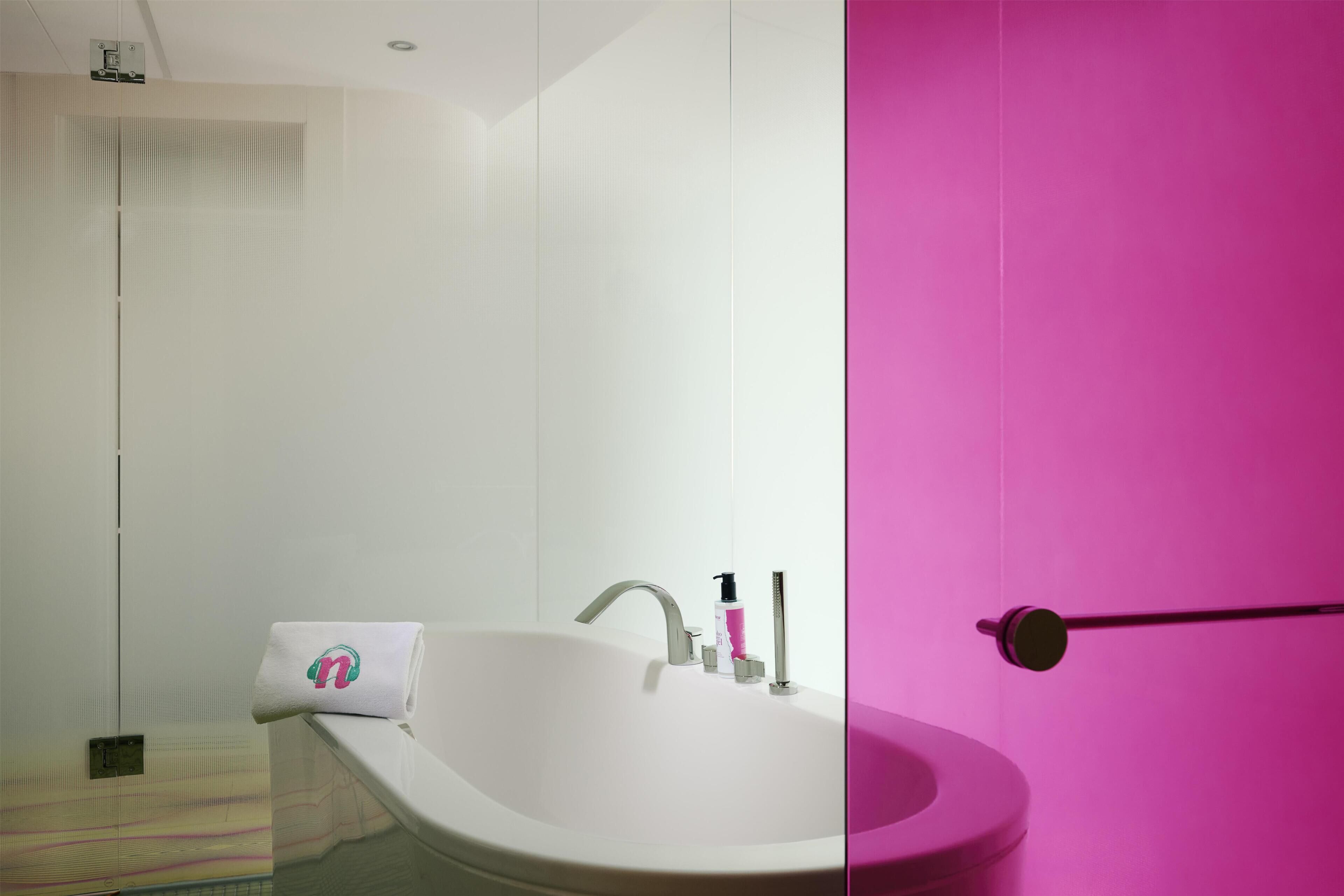 Un bagno con un lavandino bianco, un asciugamano con un logo e una parete rosa.