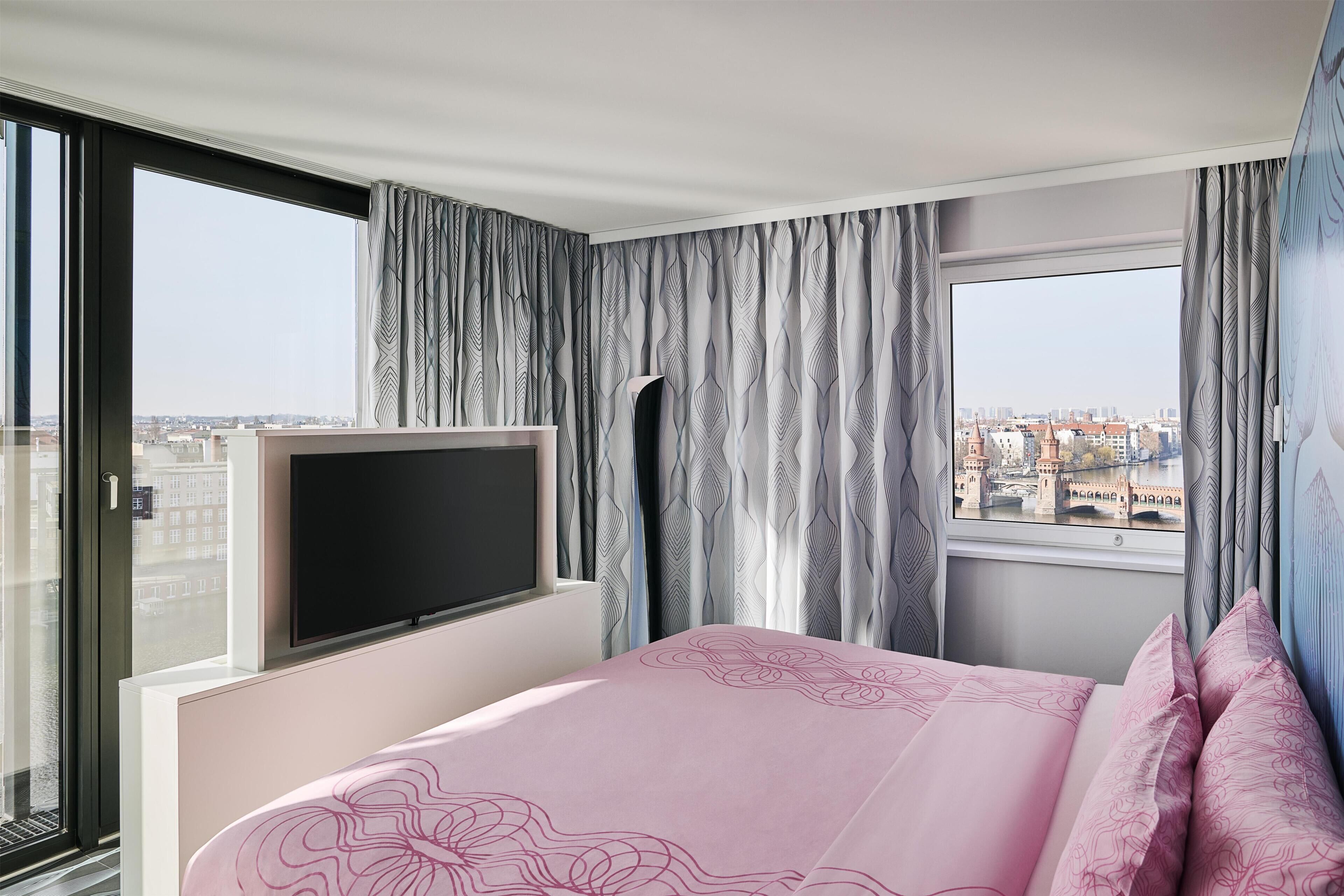 A hotel room with a bed, a TV, and a view of the city.