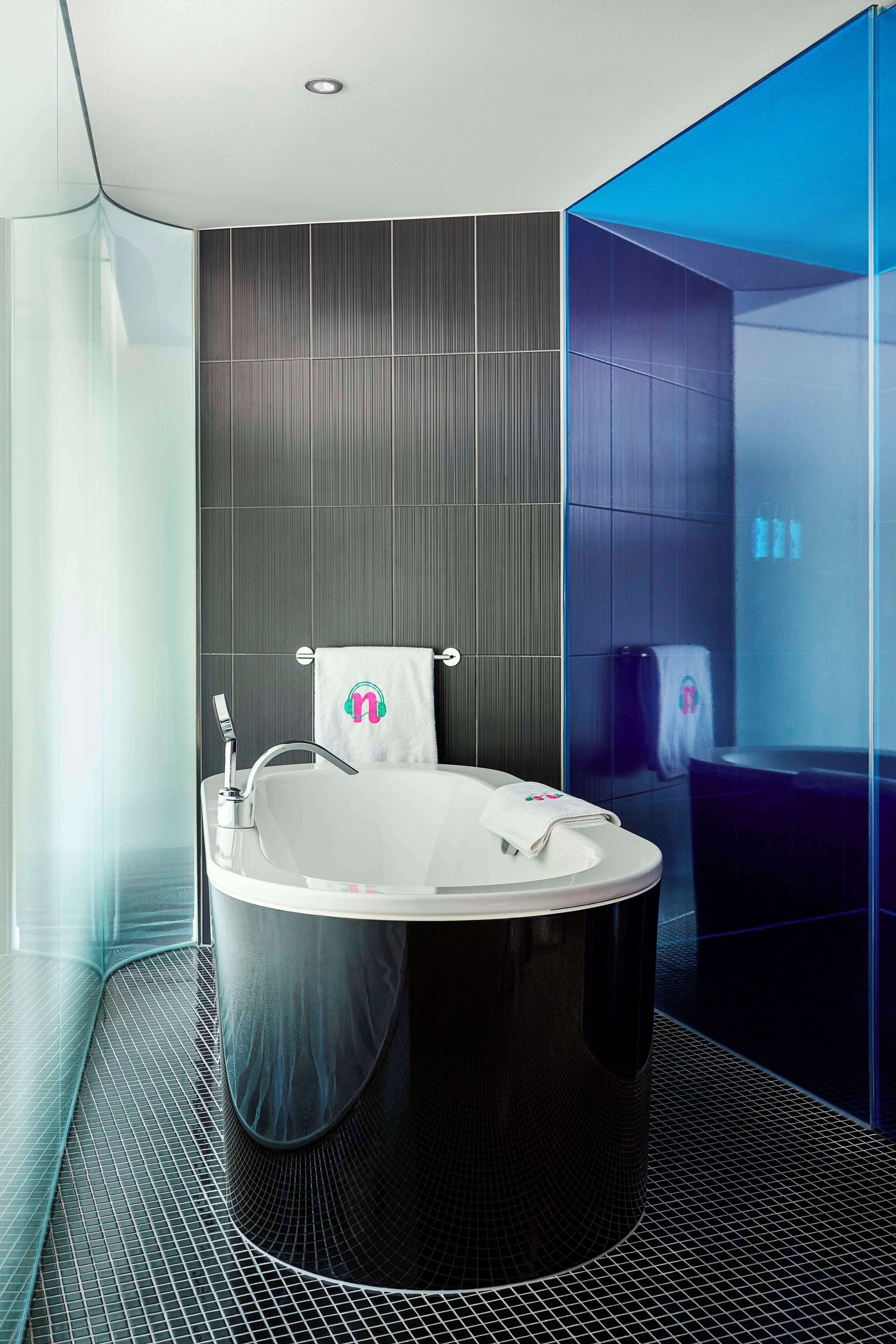 Une salle de bain moderne avec une baignoire sur pieds, une douche à parois de verre et un mur recouvert de carreaux foncés.