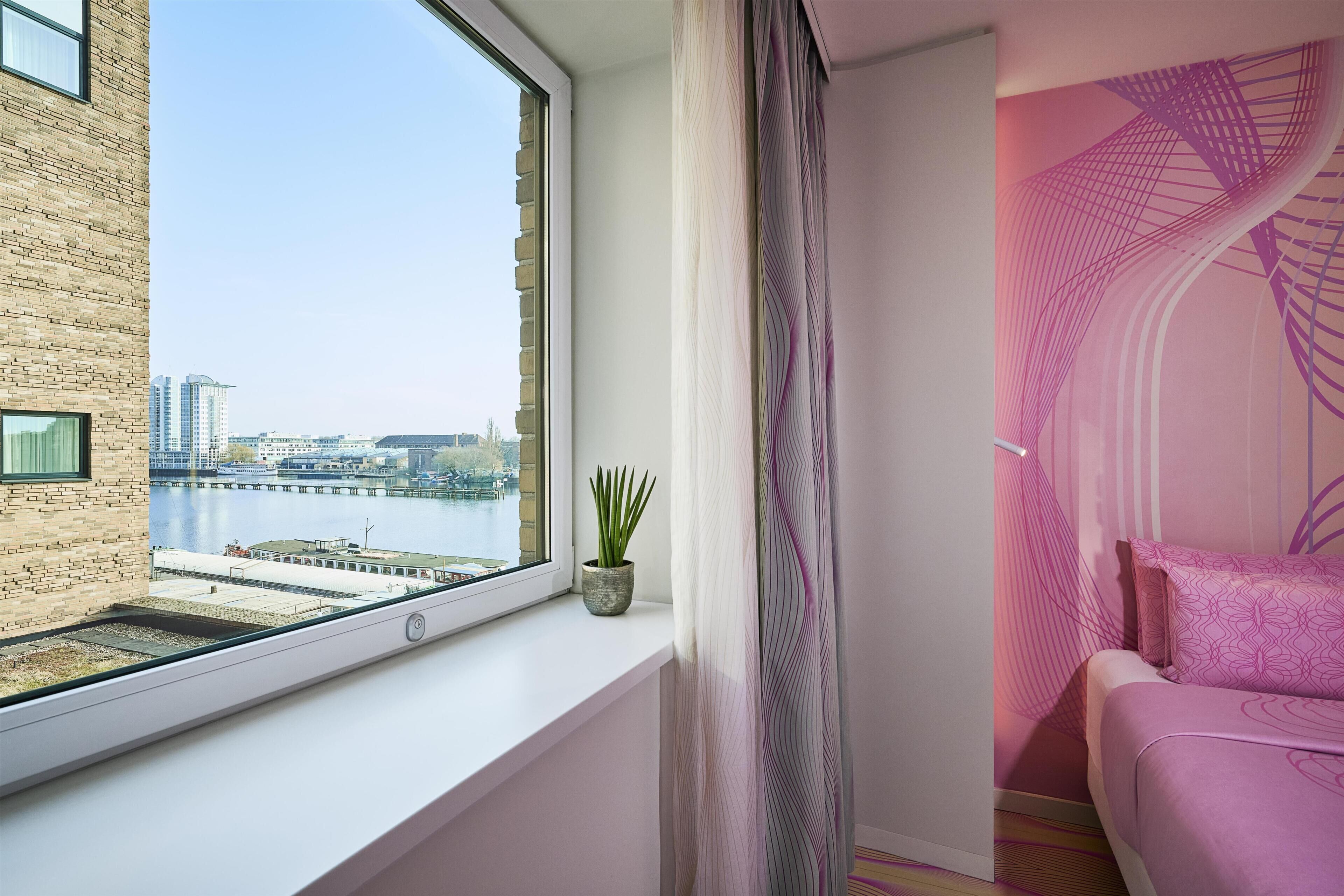 Een moderne kamer met een groot raam, uitzicht op een stadsbeeld, een potplant en een bed met behang.