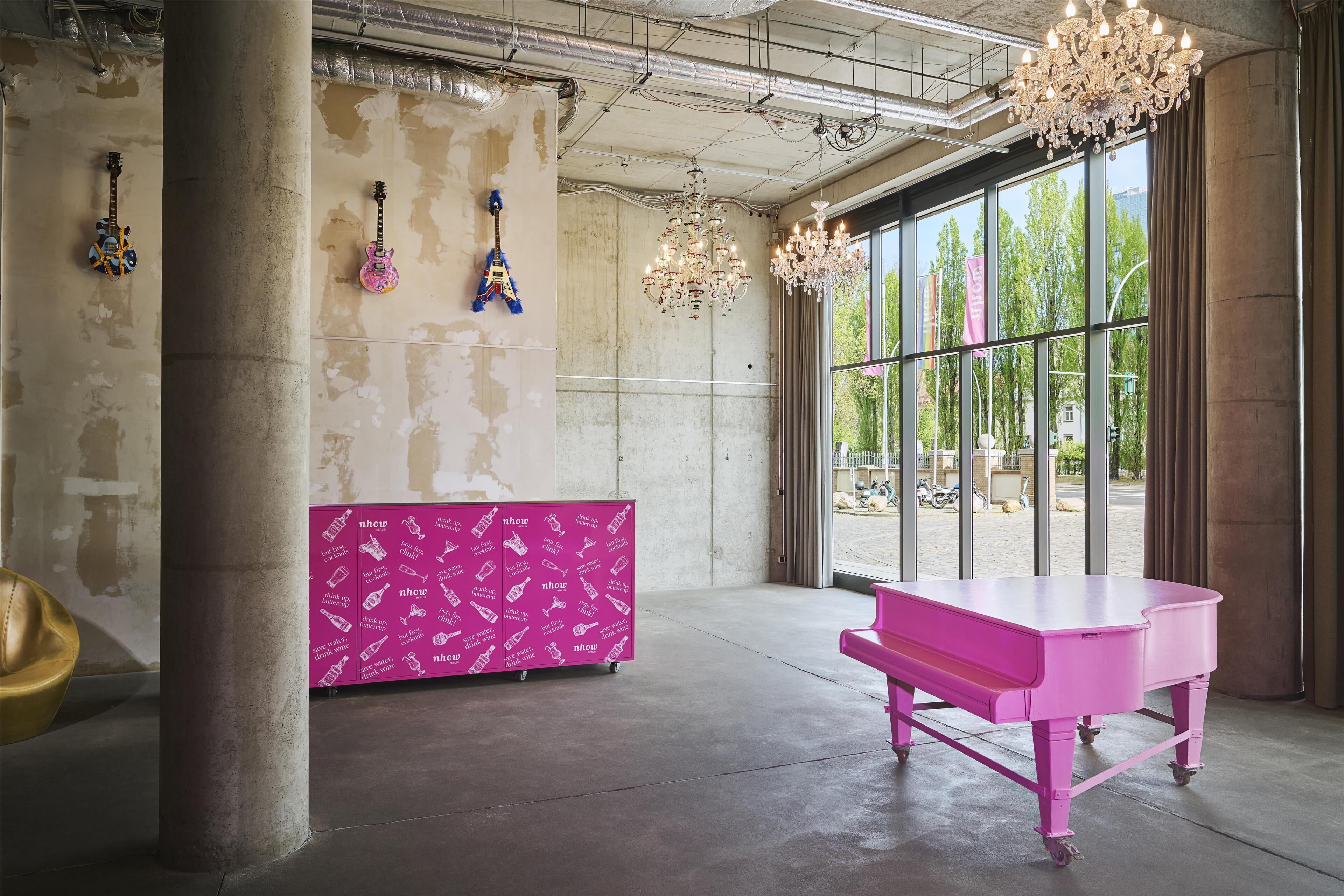 Una habitación amplia con un gran ventanal, un piano rosa y un aparador rosa con varios objetos.