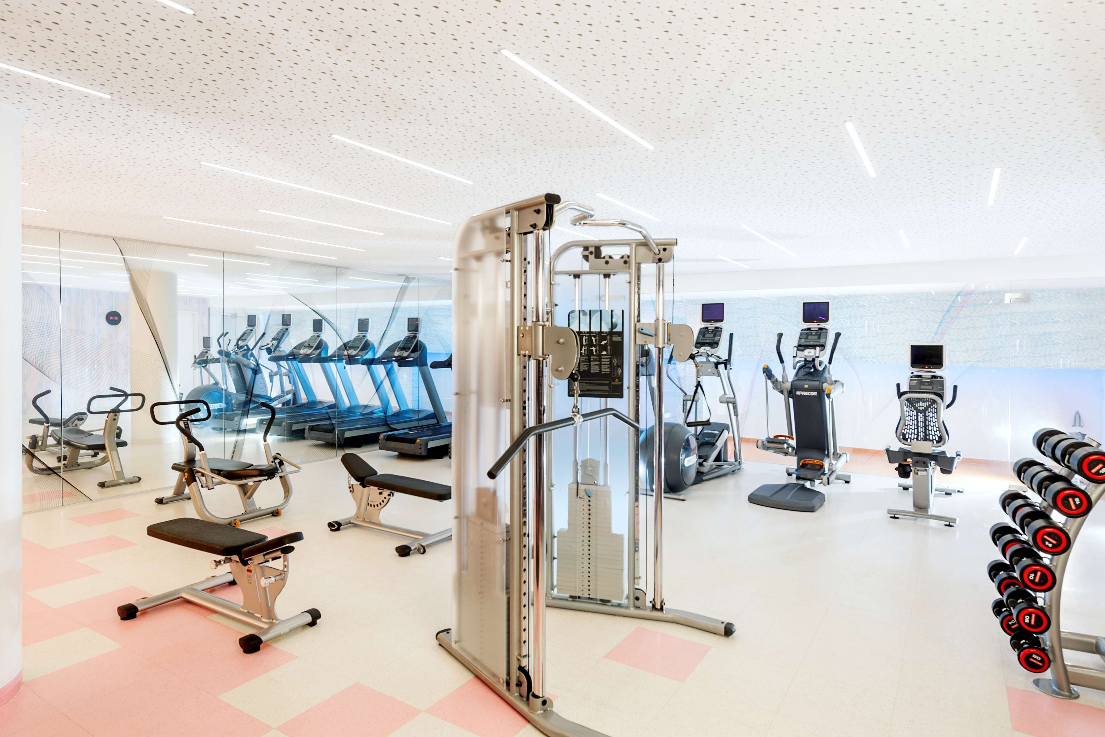 Un gimnasio moderno con diversos equipos de ejercicio, incluyendo cintas de correr, máquinas de pesas y una prensa de banca.