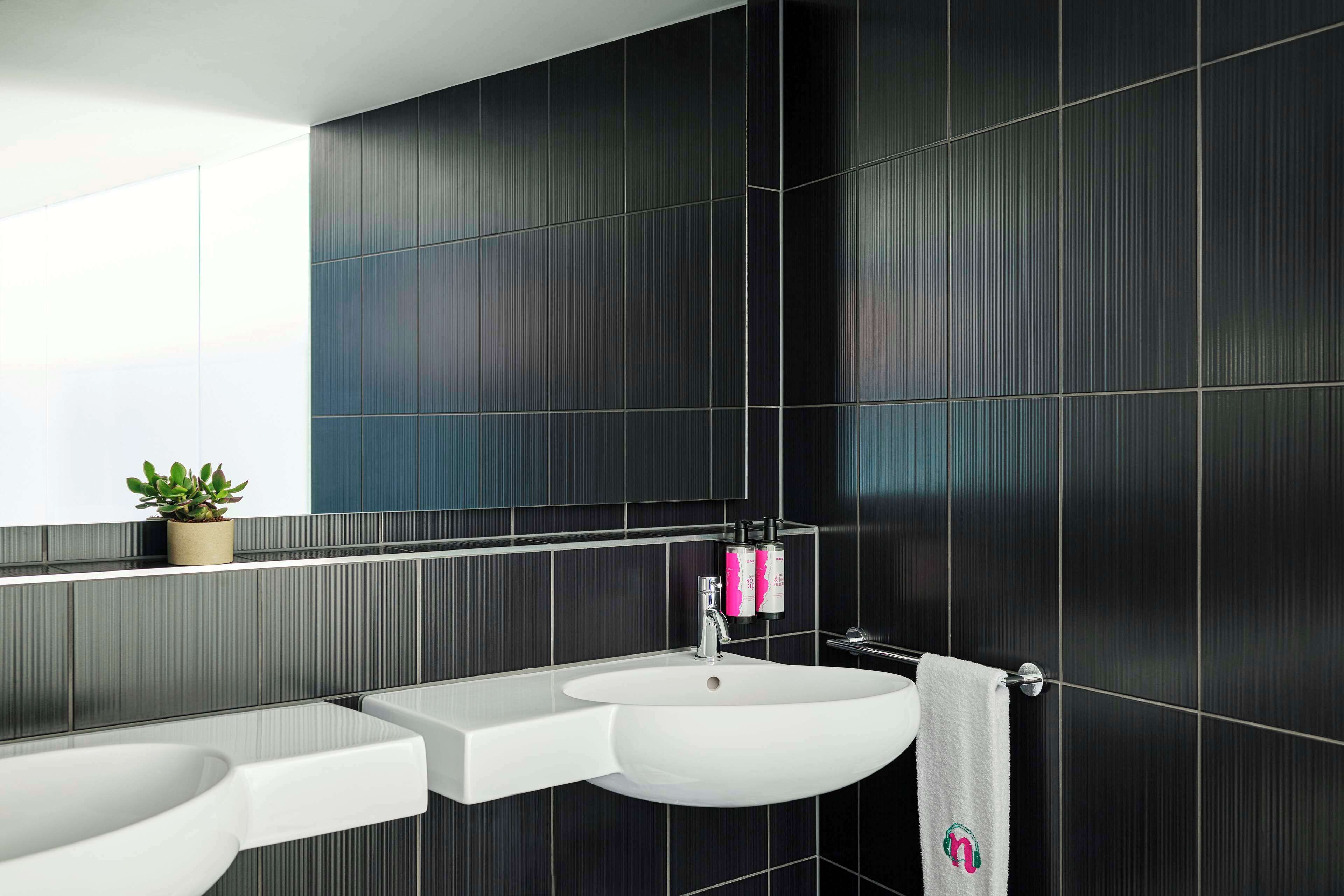 Un baño moderno con paredes de azulejos oscuros, un lavabo blanco y un espejo encima.