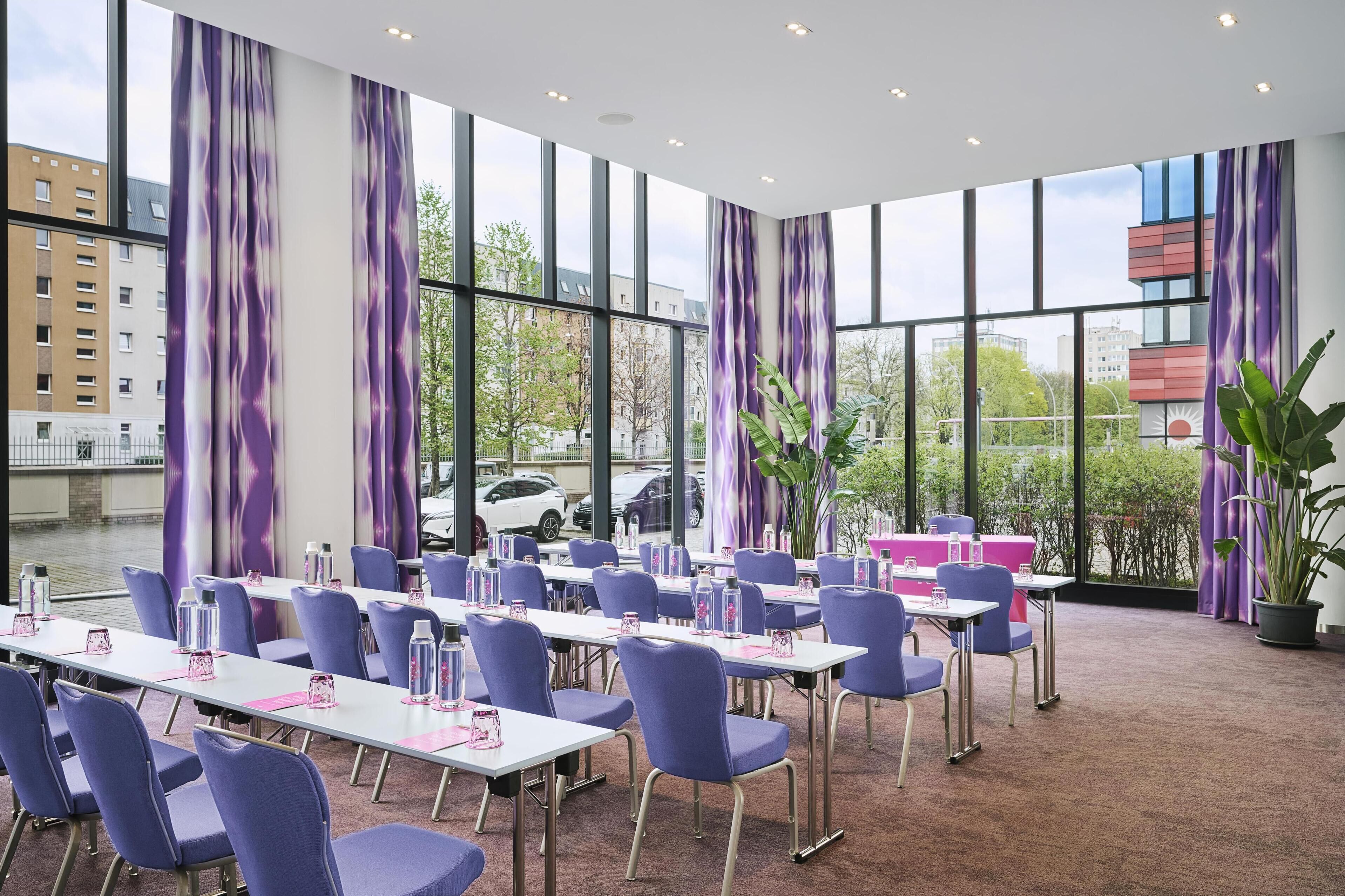 A conference room with large windows, purple curtains, and a view of buildings and trees.