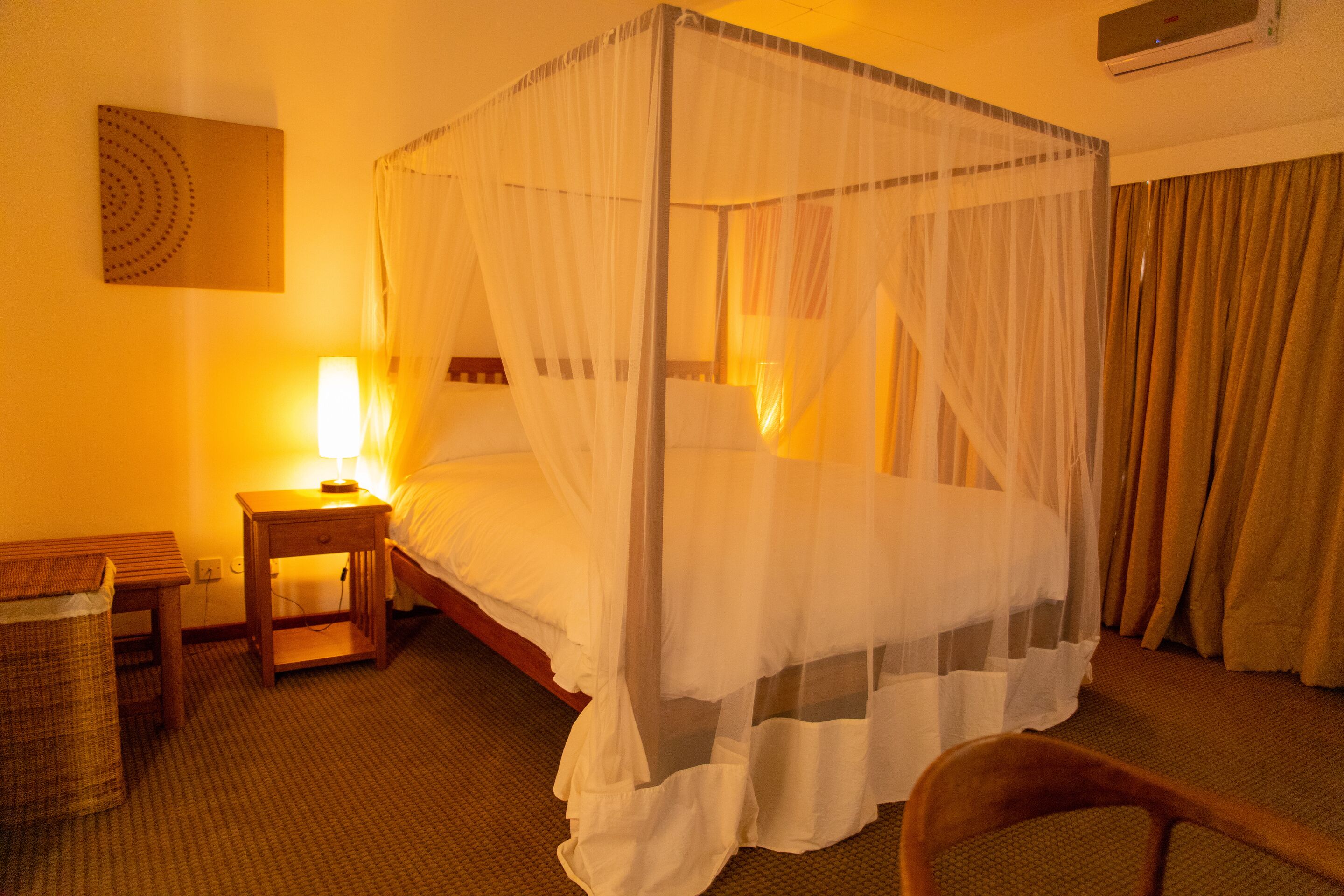 A hotel room with a four-poster bed, a bedside table with a lamp, and a chair.