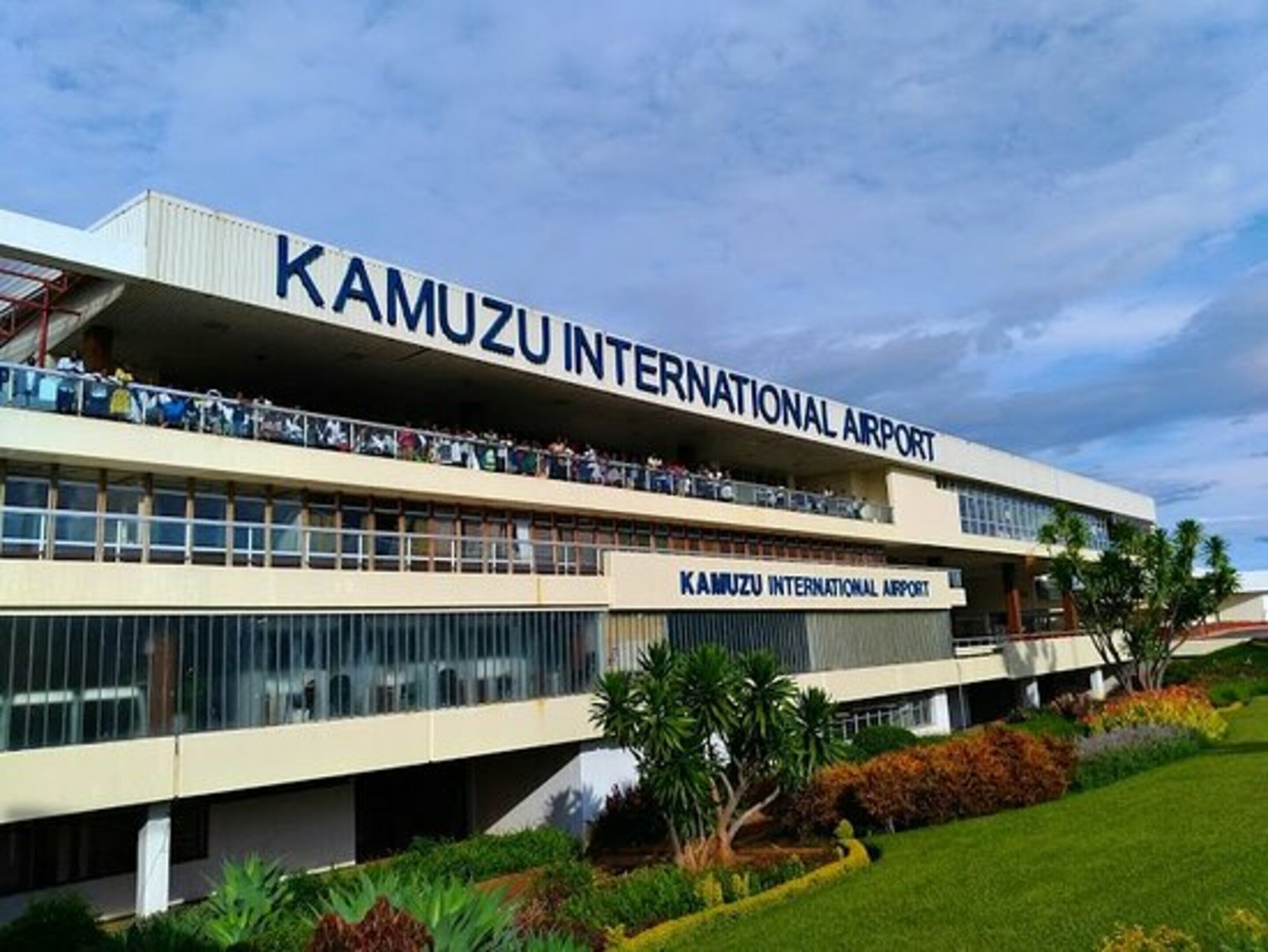 Un bâtiment moderne sur lequel on peut lire l’inscription « AÉROPORT INTERNATIONAL KAMUZU », ce qui indique qu’il s’agit d’un aéroport.