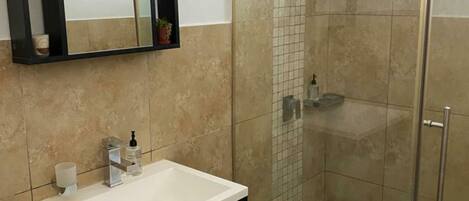 Un baño con cabina de ducha de vidrio, tocador con espejo y lavamanos.