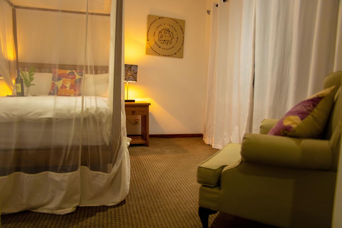 Una habitación de hotel con una cama, una mesita de noche, una lámpara, una silla y una obra de arte en la pared.