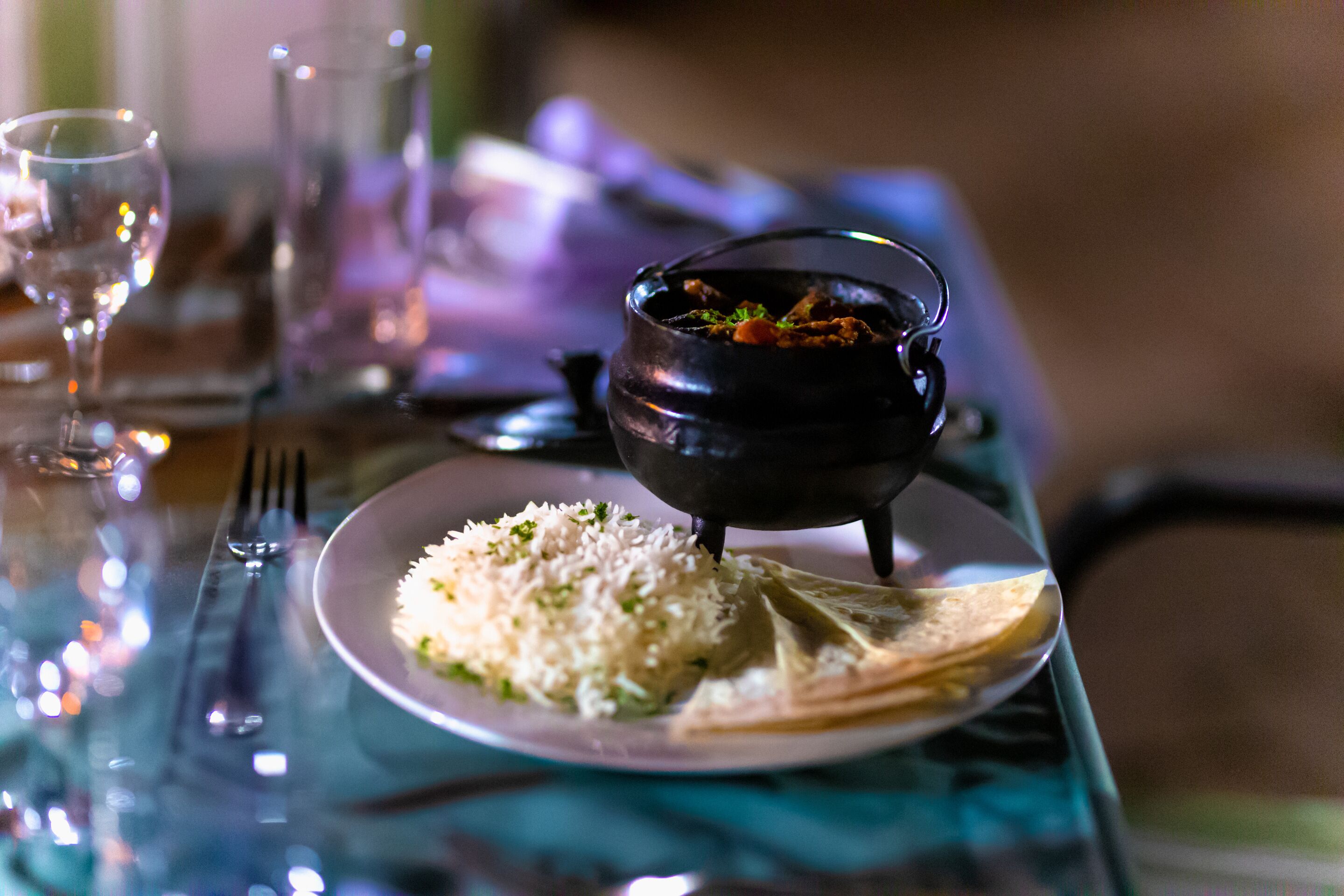 A dining table with a plate of rice, a black pot, and a glass of water.