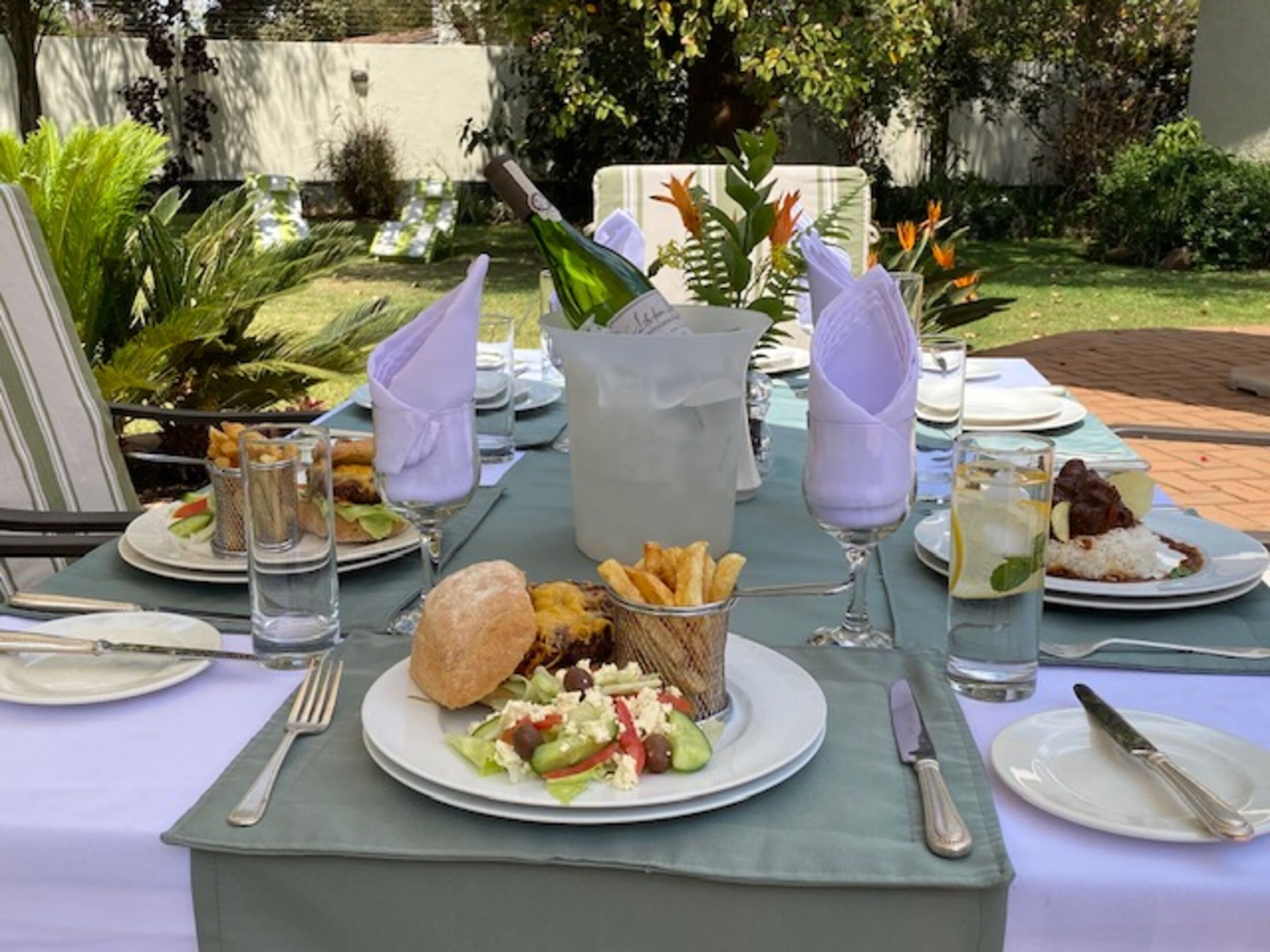 An outdoor dining setup with a table set for a meal, including plates, cutlery, and a pitcher of water.