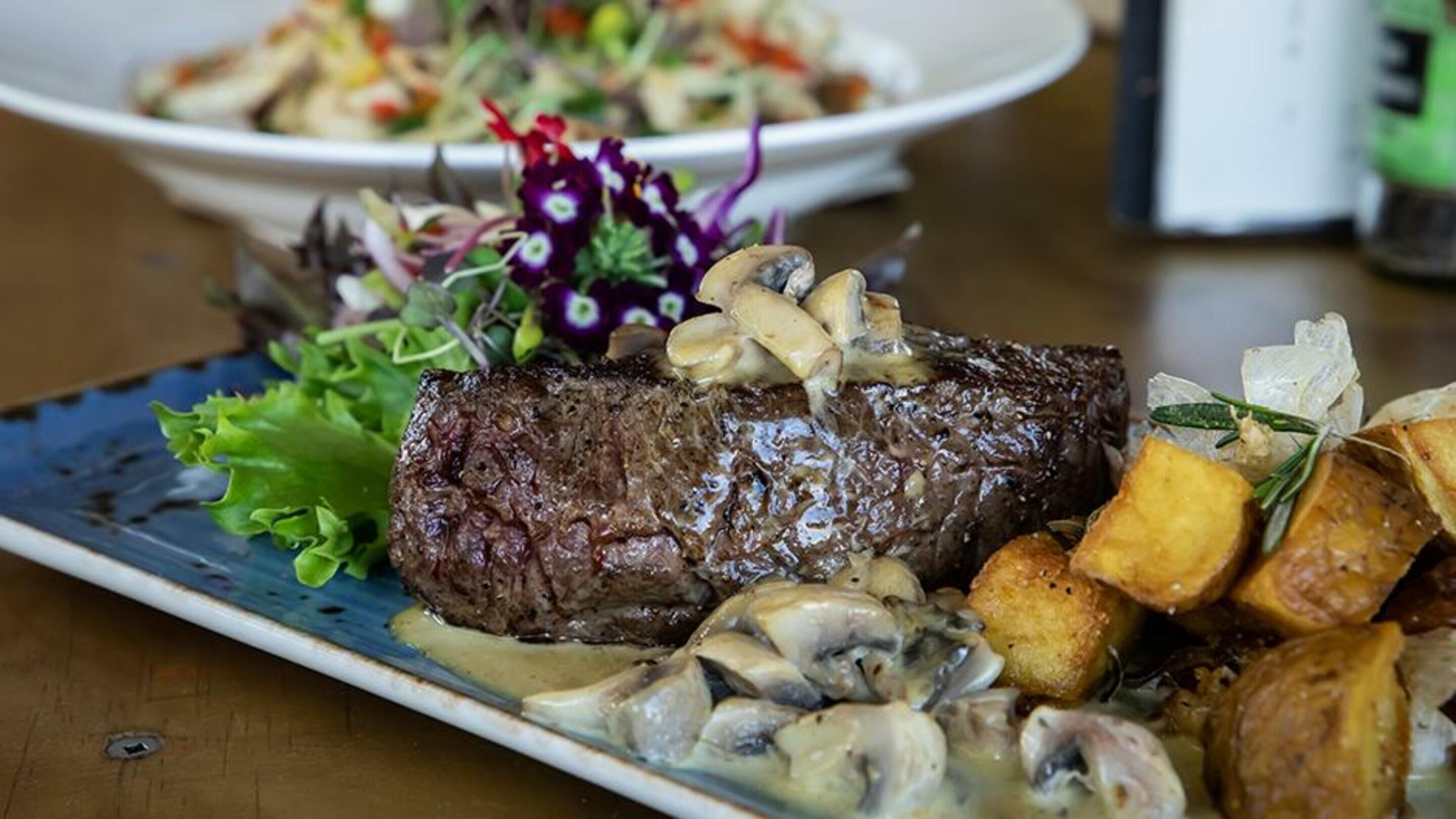 A plate with a steak topped with mushrooms and a side of roasted potatoes.