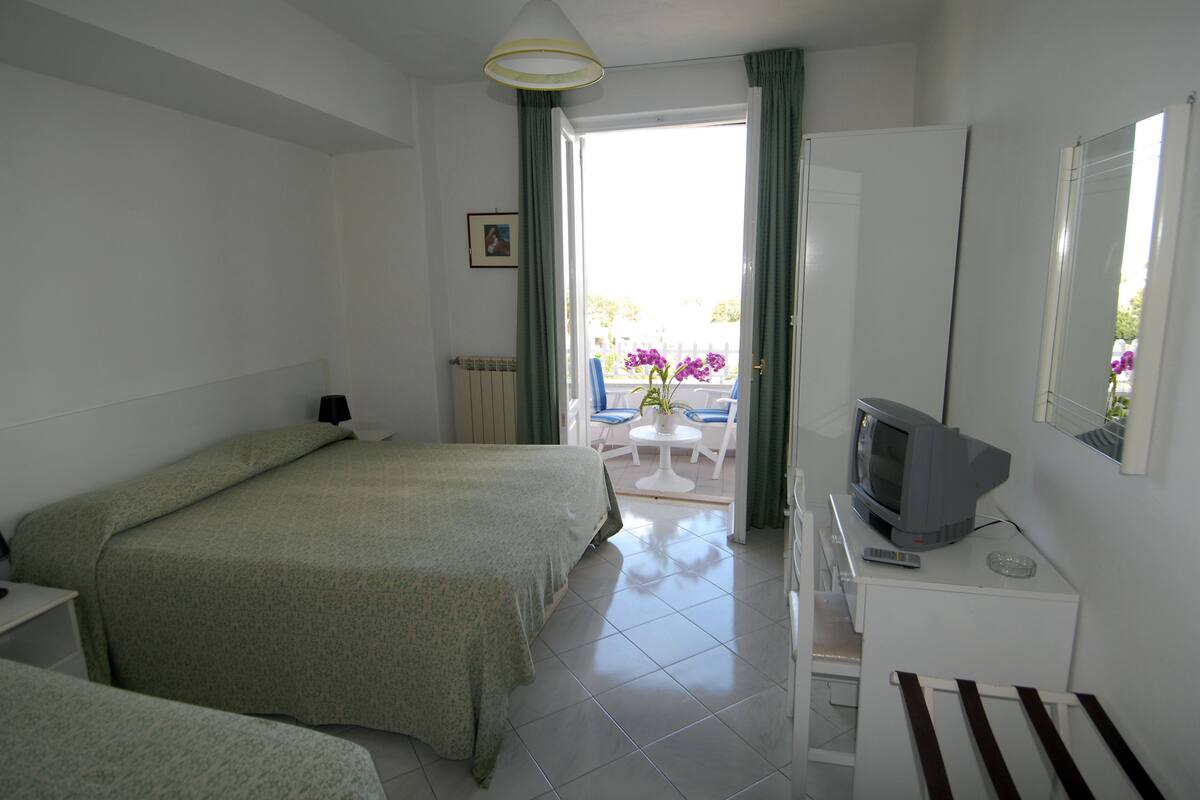 Une chambre d’hôtel avec deux lits, une télévision, une petite table avec des chaises et un balcon avec vue.