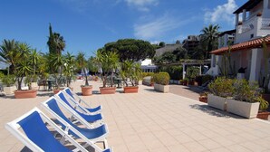 A terrace with blue lounge chairs, potted plants, and a building with a tiled roof. - Hotel Terme Colella (Forio)