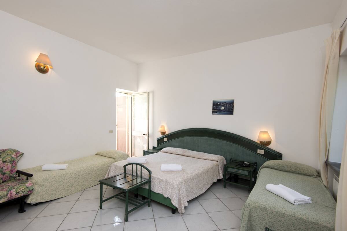 Une chambre d’hôtel avec deux lits simples, une petite table, une chaise et un bureau avec une lampe.
