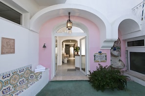 Un pasillo con pared rosa, un banco de azulejos y una maceta decorativa.