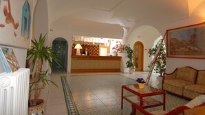 A spacious lobby with a reception desk, a sofa, a coffee table, and potted plants. - Hotel Terme Colella (Forio)
