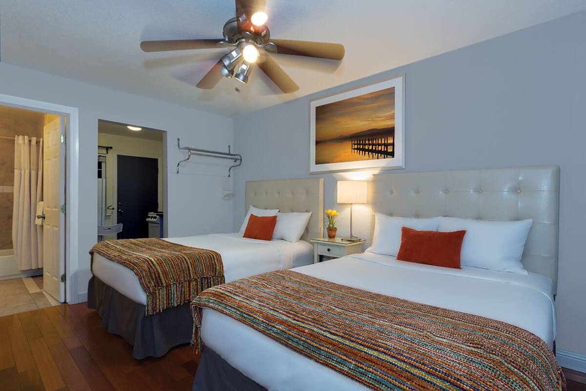 A hotel room with two beds, a ceiling fan, a framed picture on the wall, and a bathroom visible through an open door.