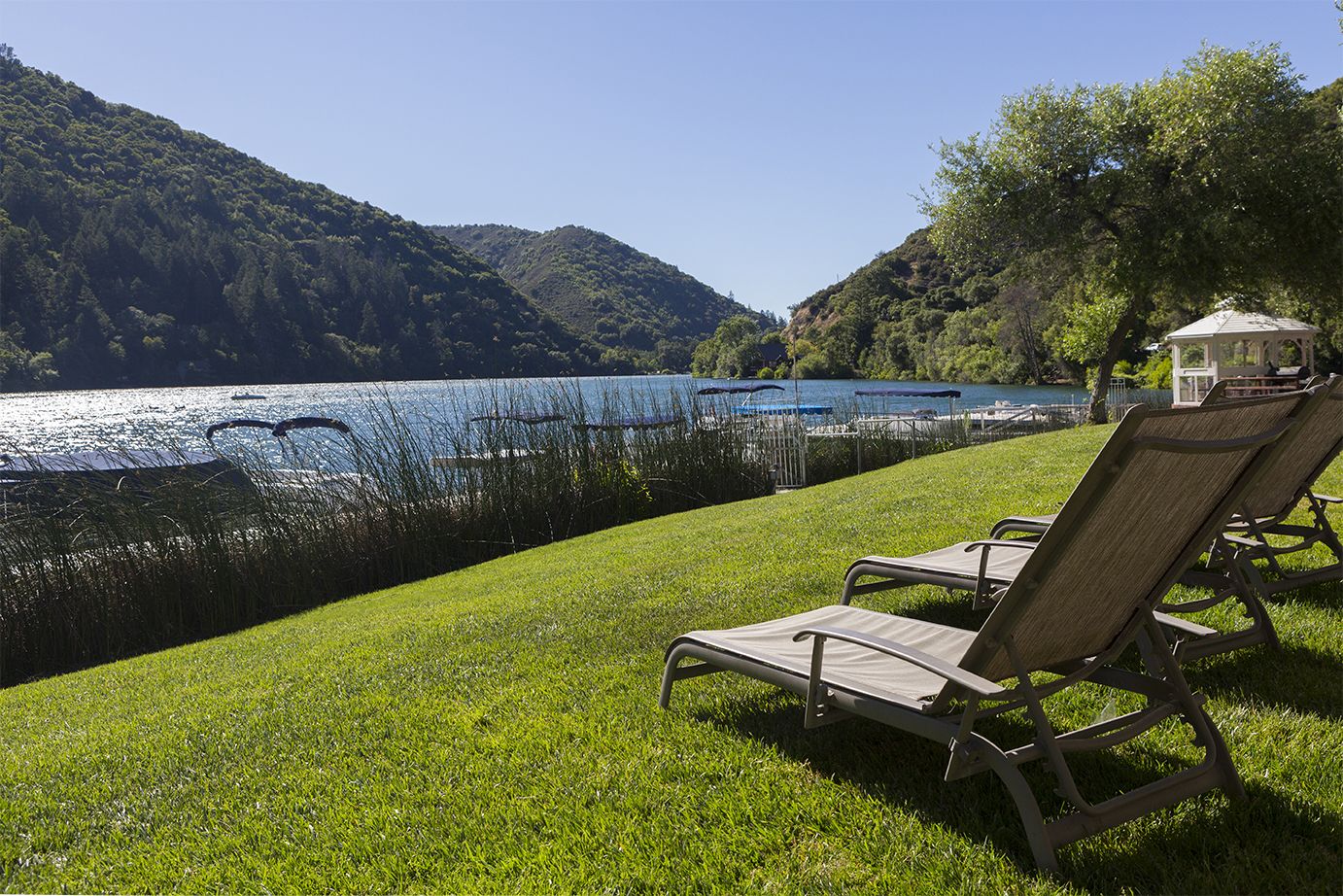 Une zone herbeuse avec deux chaises longues donnant sur un lac, entourée d’arbres et de collines.
