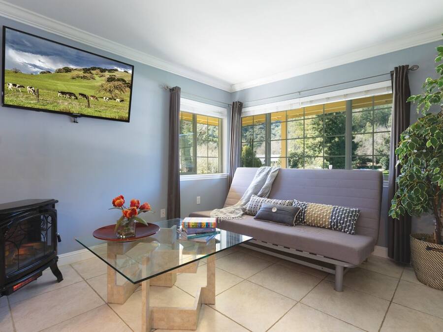 Una sala de estar con una mesa de centro de vidrio, un sofá, una chimenea y un ventanal con cortinas.