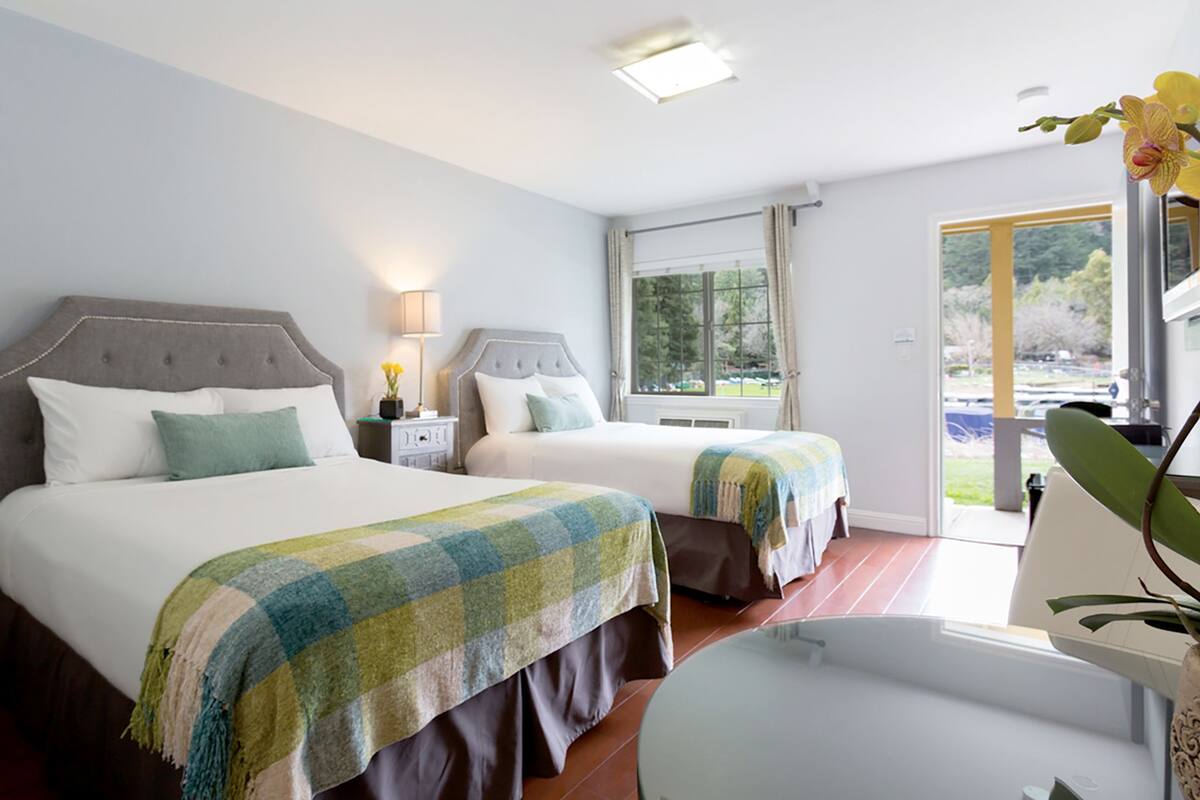 A hotel room with two beds, a sitting area, and a view of the outdoors.