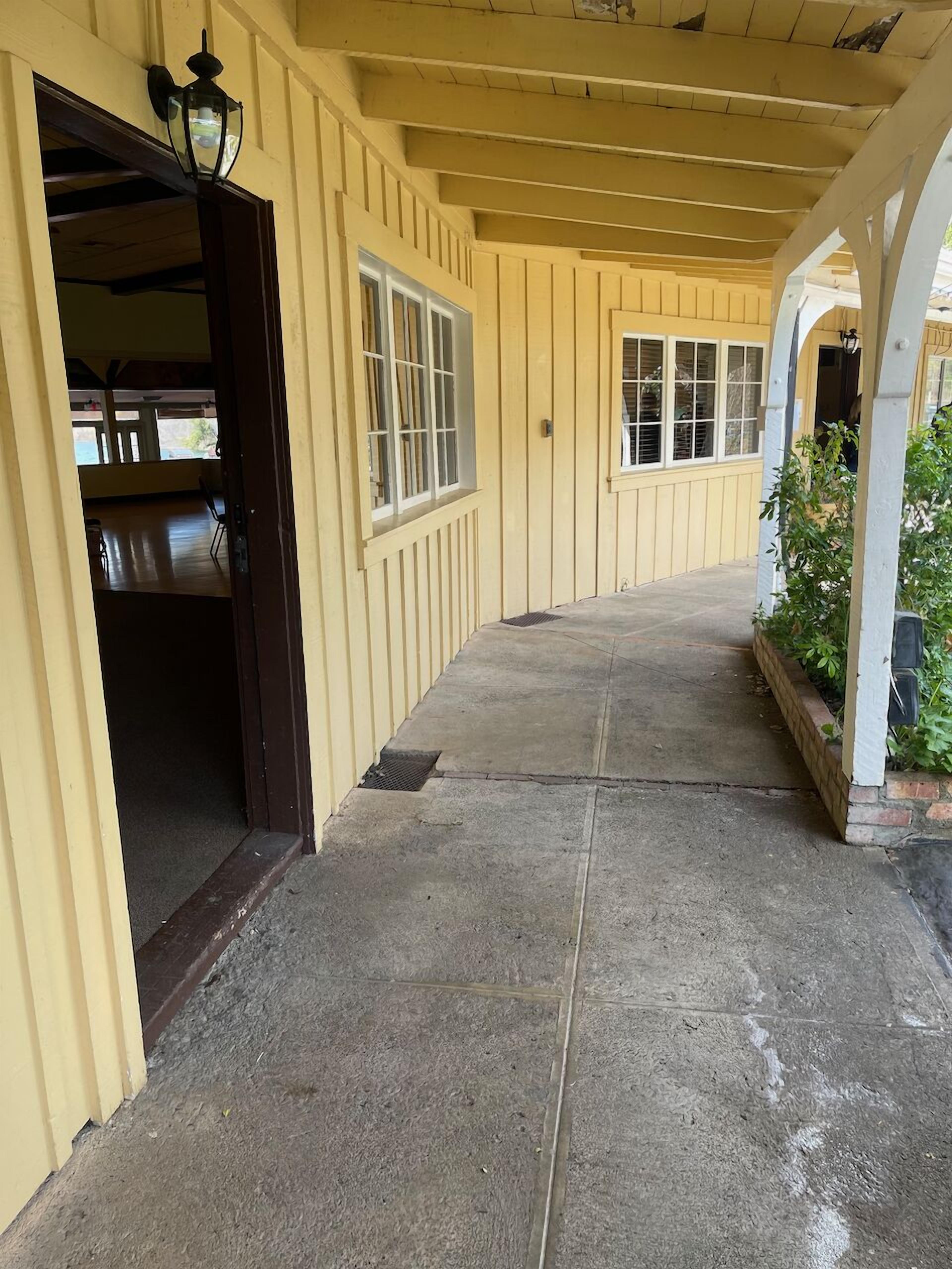 A covered walkway with a concrete floor, wooden railings, and a door leading to an interior space.