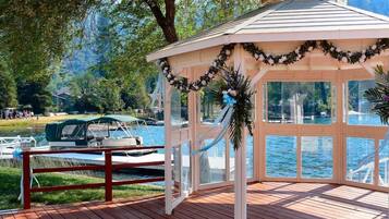A gazebo with a wooden deck, surrounded by a lake and trees.