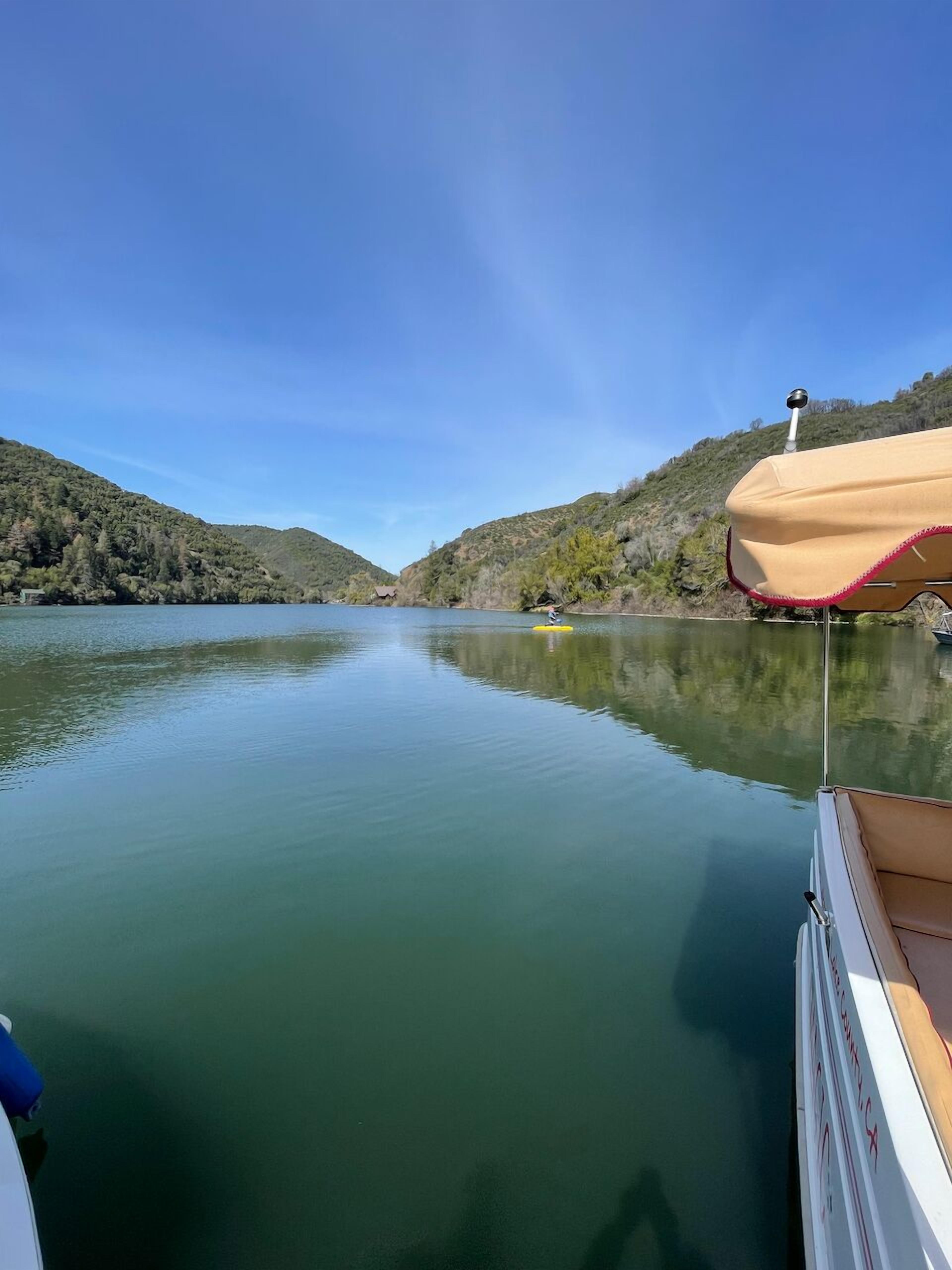 A calm lake with a boat docked on the right, surrounded by hills and a clear sky.