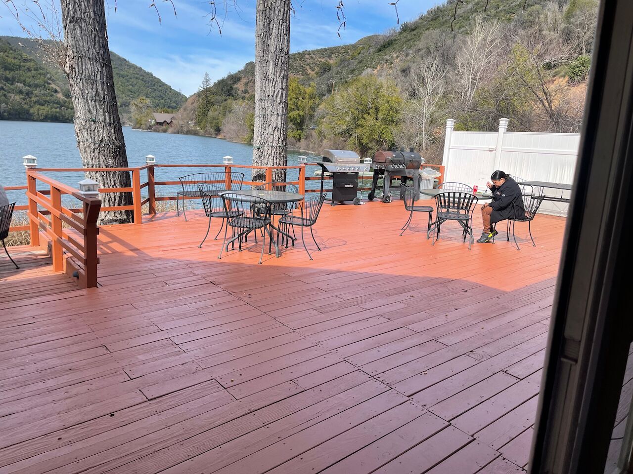 Terraza de madera con mobiliario exterior, con vistas a un lago y colinas.