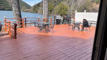 Um deck de madeira com área de estar externa, com vista para um lago e colinas.