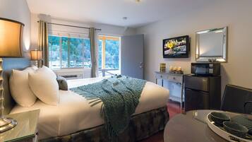 Una habitación de hotel con cama, mesita de noche, lámpara, televisión y un área de comedor con mesa y sillas.