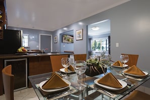 Uma área de jantar moderna com mesa de vidro posta para quatro pessoas, com guardanapos dourados e copos de vidro transparente.
