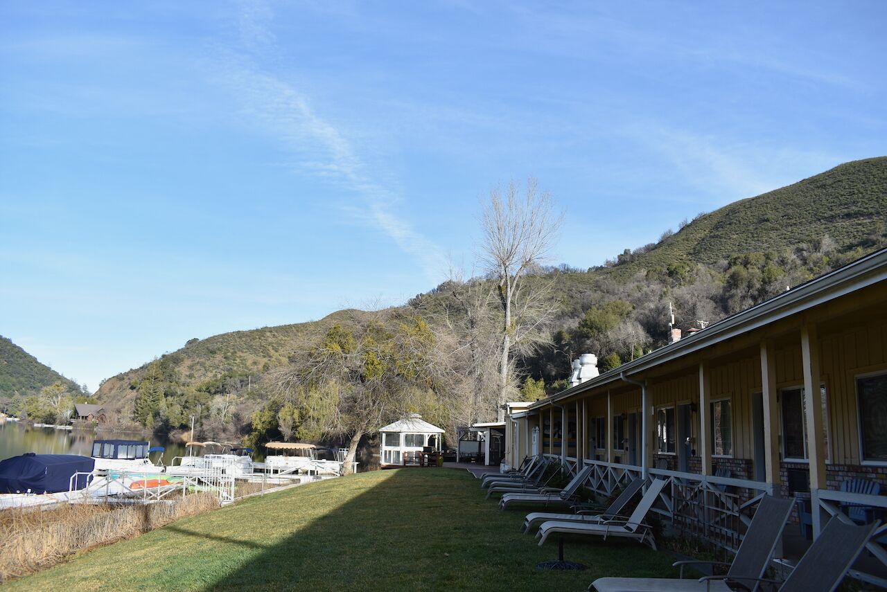 A resort with a pool, lounge chairs, and a view of a lake and hills.