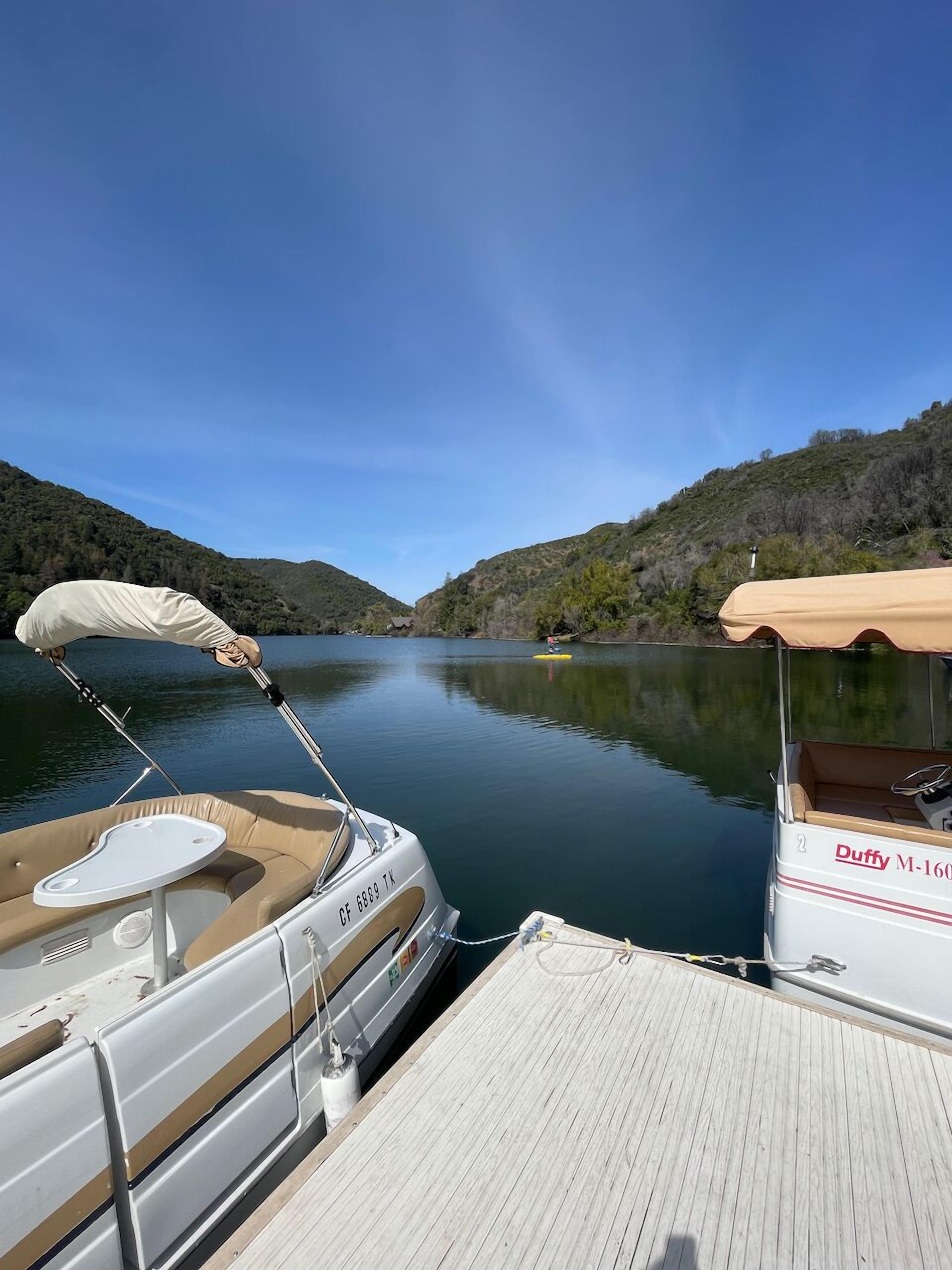 A boat docked at a calm lake with a forested hillside in the background.