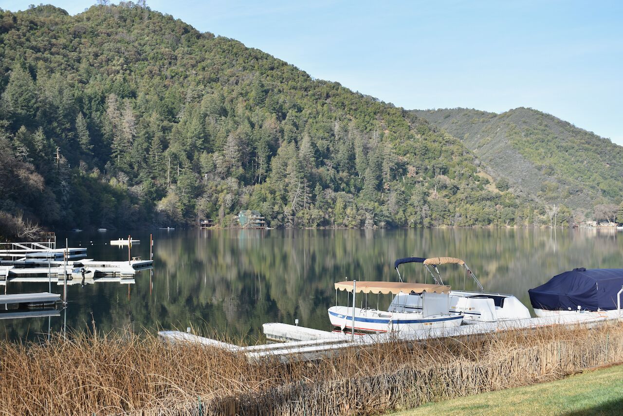 A calm lake with docked boats, surrounded by forested hills.