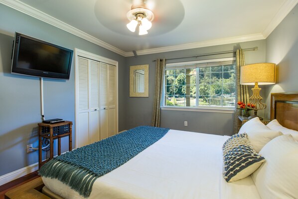 A bedroom with a large bed, a television mounted on the wall, a window with curtains, and a ceiling fan. - The Lodge At Blue Lakes (Upper Lake)